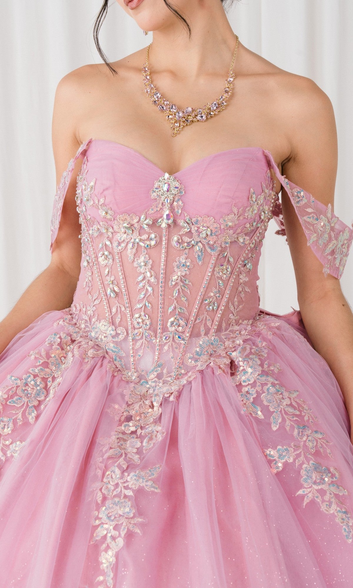 A woman wears the Quinceanera Dress 8405JQ By Cinderella Couture, a pink ball gown with floral embroidery, bead accents, and an ornate necklace, set against a white background.
